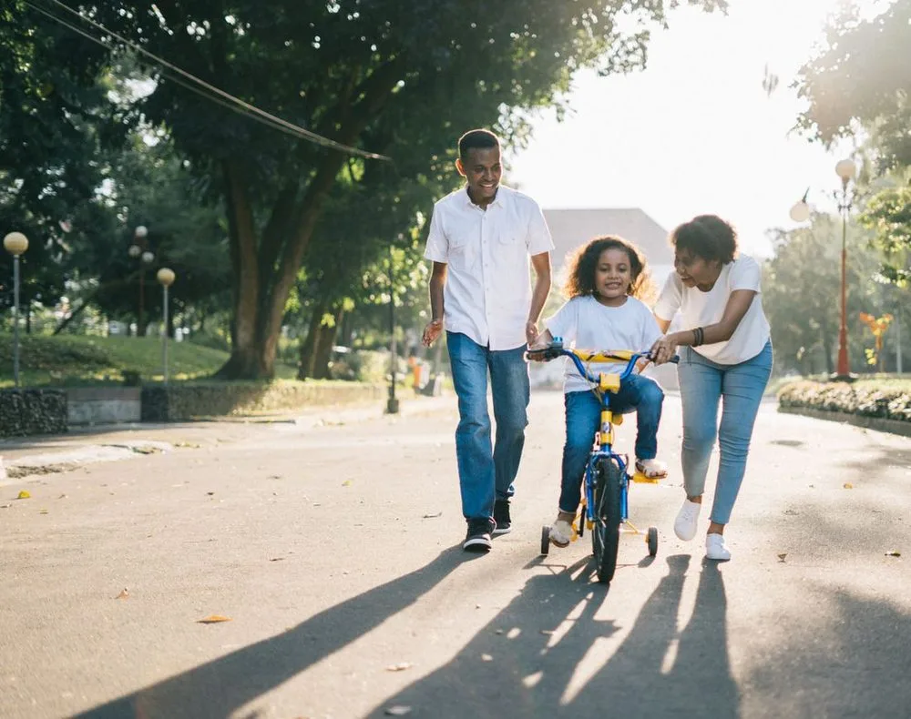 Parents teaching their daughter to ride a bike in a sunlit park